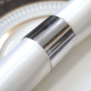 Detail of silver metallic napkin ring with mirror finish on white napkin and ceramic plate