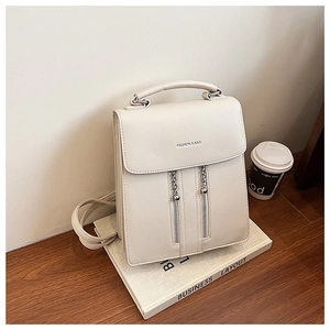 Close-up of cream PU leather backpack with荔枝 texture and dual metal zippers on wooden desk
