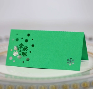 Green snowflake laser-cut place card displayed on a white plate for Christmas dinner decor