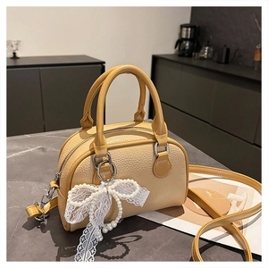 Detail of ginger yellow lychee pattern Boston bag with pearl lace bow charm on a counter