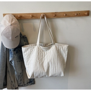 Detail of beige pleated tote bag with JUMAITU logo hanging on a wooden coat rack