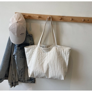 Detail of white pleated tote bag with thin straps and brand label on a minimal wall