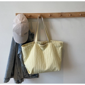 Detail of light yellow pleated tote bag hanging on wooden hook with brand patch
