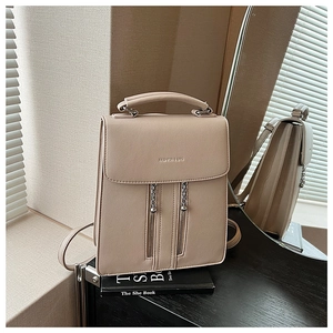 Detailed view of beige leather backpack with decorative zippers and silver chain detail