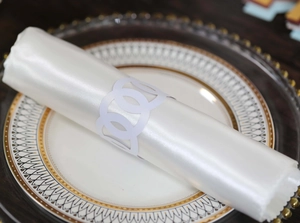 Detail of interlocking white hollow napkin ring with satin napkin on elegant plate