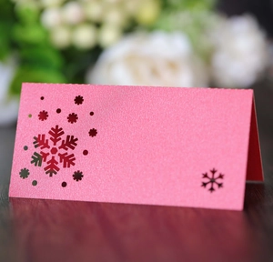 Pink pearl paper place card with laser-cut snowflake detail on dark wooden surface