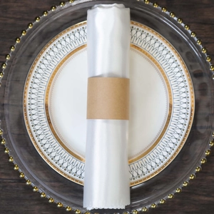 Close-up of white satin napkin rolled with a minimalist kraft paper sleeve on a dinner plate