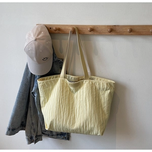 Detail of light yellow tote bag with pleated texture hanging on a wooden rack