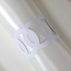 Detail of white laser-cut geometric napkin ring on smooth white satin fabric roll