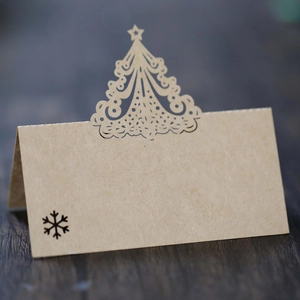 Detail of kraft paper place card featuring a laser-cut Christmas tree on a wood background