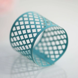 Close-up of laser-cut teal paper napkin ring with a geometric diamond mesh pattern