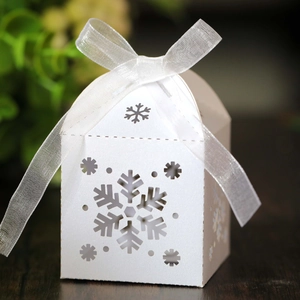Detalle de la caja de regalo blanca en forma de casa con copos de nieve calados y cinta