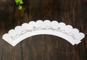 Flat lay view of white scalloped cupcake wrapper with Cake Play artistic print on wood