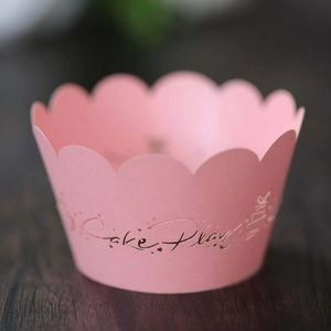 Close-up of pink scalloped cupcake wrapper with Cake Play print on dark wood
