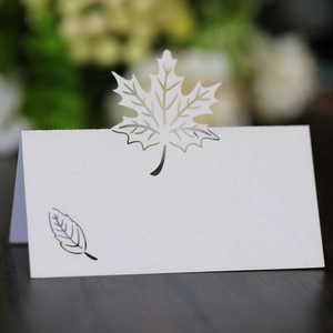 Detail of white laser-cut maple leaf place card with pearlescent finish on wooden table