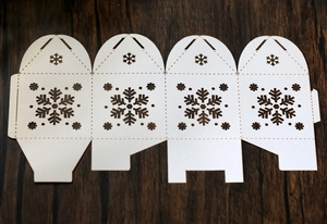 Detalle de copos de nieve cortados con láser en caja de regalo blanca sobre fondo de madera