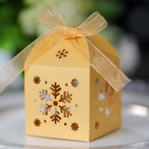 Primer plano de caja de regalo dorada con copos de nieve láser y lazo de organza