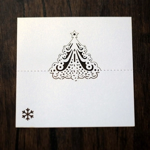 Detail of white laser-cut Christmas tree place card with snowflake on wood background