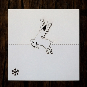 Detail of white laser-cut reindeer and snowflake place card on dark wood table