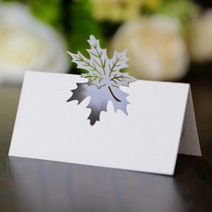 Detail of white laser-cut maple leaf place card with elegant hollow design for weddings