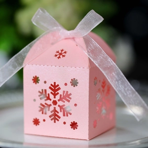 Vista detallada de caja de regalo rosa nacarada con copo de nieve calado y lazo de organza