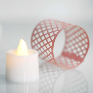 Macro focus on warm LED tea light flame with pink laser-cut hollow paper lampshade