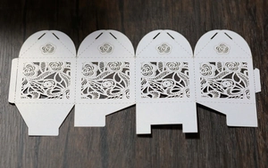 Flat lay of white laser-cut rose hollow favor box template on dark wood background