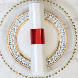 Close-up of a glossy red napkin ring on a white napkin over a decorative gold-rimmed plate