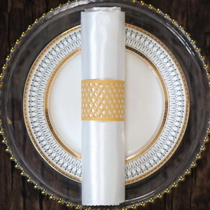Close-up of golden laser-cut hollow grid napkin ring on white satin on elegant plates