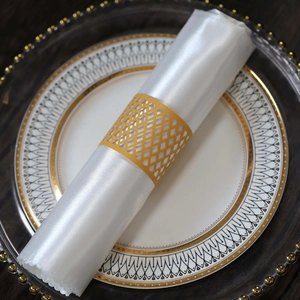 Detail of laser-cut gold lattice napkin ring on white satin fabric and luxury plate