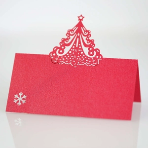 Detail of red Christmas place card with laser-cut tree and snowflake patterns on white surface