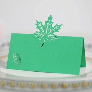 Detailed close-up of a laser-cut green maple leaf place card on a white dinner plate