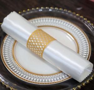 Close-up of golden hollow grid napkin ring on a white silk napkin and elegant plates