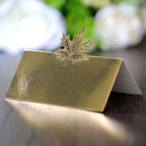 Macro shot of laser-cut gold maple leaf place card on a rustic wood surface