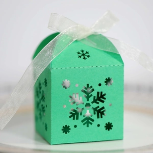 Detalle de la caja de regalo verde menta con forma de casa con motivos de nieve y cinta blanca