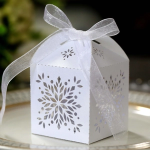 Detailed close-up of white laser-cut snowflake favor box with delicate organza ribbon bow