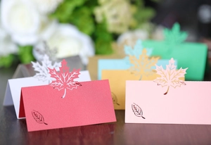 Macro detail of laser-cut maple leaf place cards in various colors on wooden surface