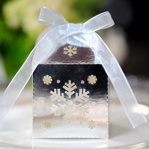 Detalle de una caja de regalo plateada cortada por láser con copo de nieve y lazo celeste