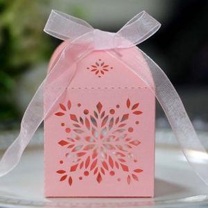 Detail of pink laser-cut snowflake candy box with white ribbon bow on white tray