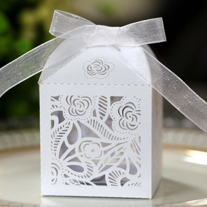 Close-up of laser-cut white rose favor box with a white organza ribbon bow on a plate