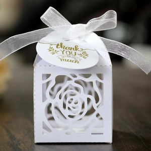 Detail of white laser-cut rose candy box with ribbon and thank you tag on wood surface