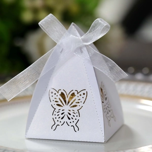 Detailed view of white pyramid favor box with laser-cut butterfly and ribbon on a plate