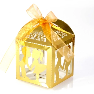 Détail boîte à bonbons de mariage dorée avec silhouettes découpées au laser et ruban organza