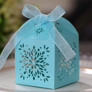 Close-up of light blue laser-cut snowflake candy box with elegant ribbon on a white plate