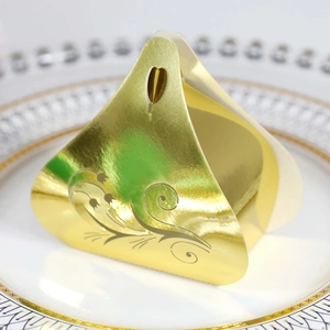 Macro shot of gold triangular wedding candy box with heart cutout and floral pattern