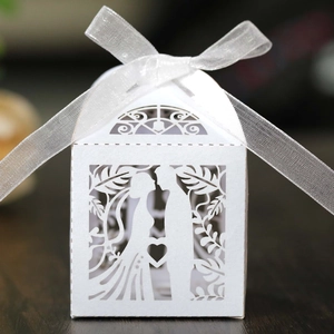 Detail view of laser-cut white wedding favor box with bride and groom silhouette and ribbon