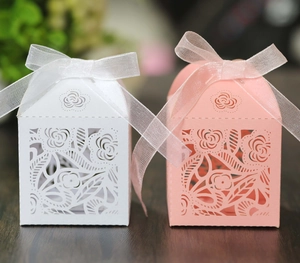 Detail of laser-cut wedding favor boxes in white and pink with floral rose pattern