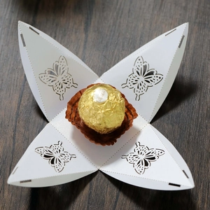 Detail view of laser-cut white butterfly favor box unfolded on wood background