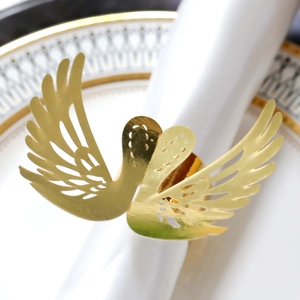 Detail of laser-cut golden swan napkin ring with intricate hollow wings on white napkin