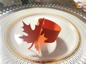 Close-up of orange maple leaf paper napkin ring on decorative plate for autumn tables